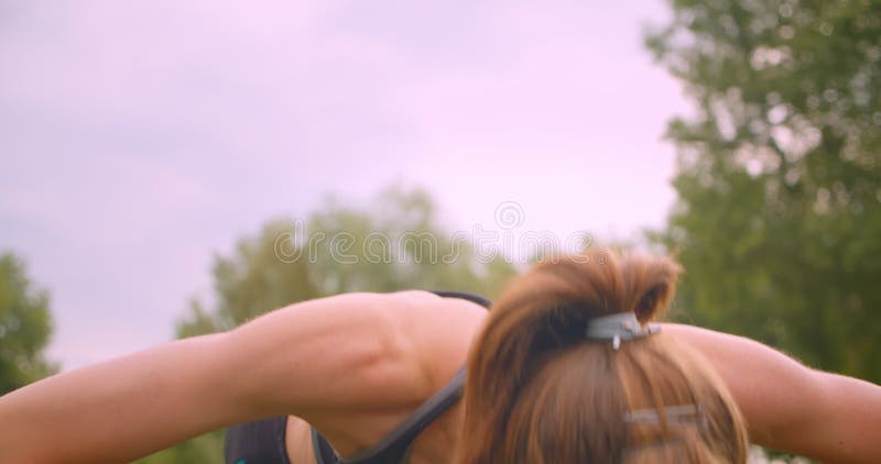 Closeup portrait of young cute sporty fitness girl making push ups in the park in urban city outdoors