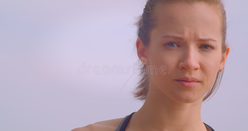 Closeup portrait of young pretty female jogger in sportswear looking forward being determined with blue sky on the