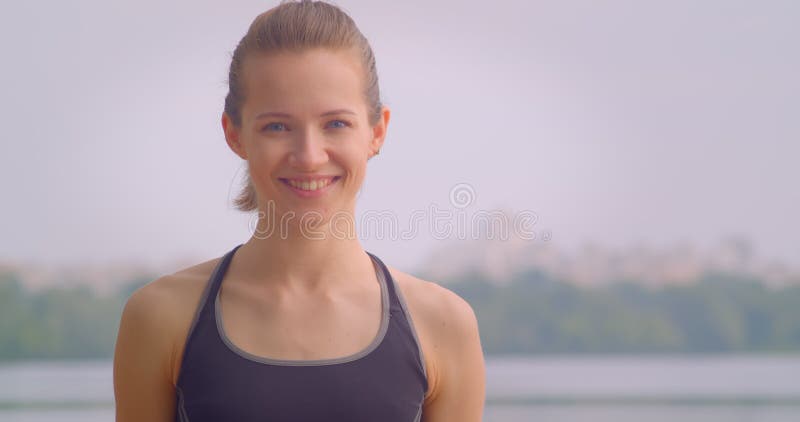 Closeup portrait of young pretty sporty female jogger looking at camera with blue sky on the background outdoors