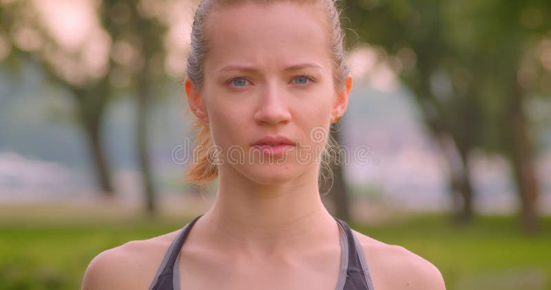 Closeup portrait of young pretty sporty female jogger looking at camera in the park in urban city outdoors