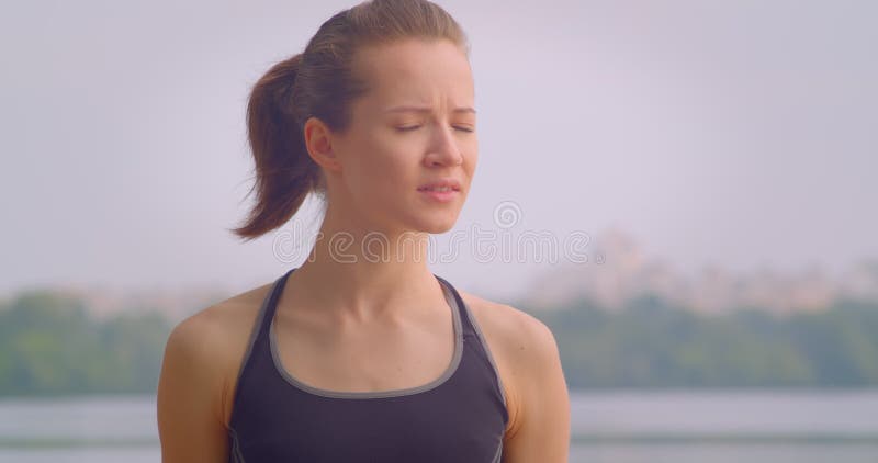 Closeup portrait of young pretty sporty female jogger looking forward with blue sky on the background outdoors