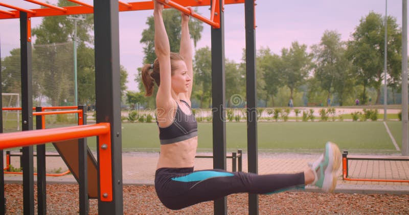 Closeup portrait of young pretty sporty fitness girl making exercises on the athletic field in urban city outdoors