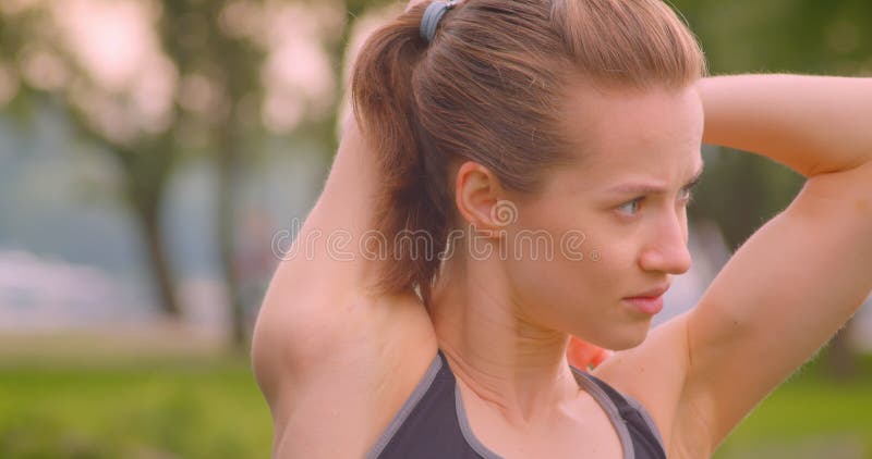 Closeup portrait of young pretty sporty fitness girl stretching her arms in the park in urban city outdoors