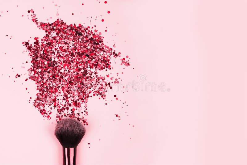 Closeup of professional cosmetic makeup brush with explosion of shiny pink colorful sparkles on bright pink background