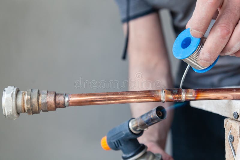 Closeup professional master plumber holding flux paste for soldering and brazing seams of copper pipe gas burner. Concept