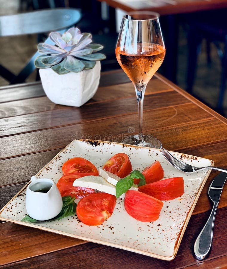 Closeup of a salad with cheese and tomatoes on a square plate with alcoholic beverage near a plant royalty free stock photography Closeup of a salad with cheese and tomatoes on a square plate with alcoholic beverage near a plant royalty free stock photography