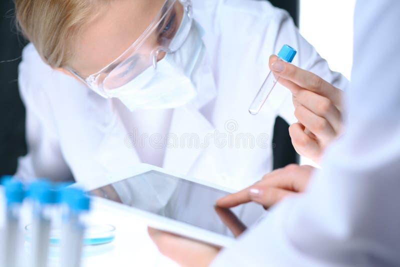 Closeup of scientific research team with clear solution in laboratory. Blonde female chemist holds test tube of glass