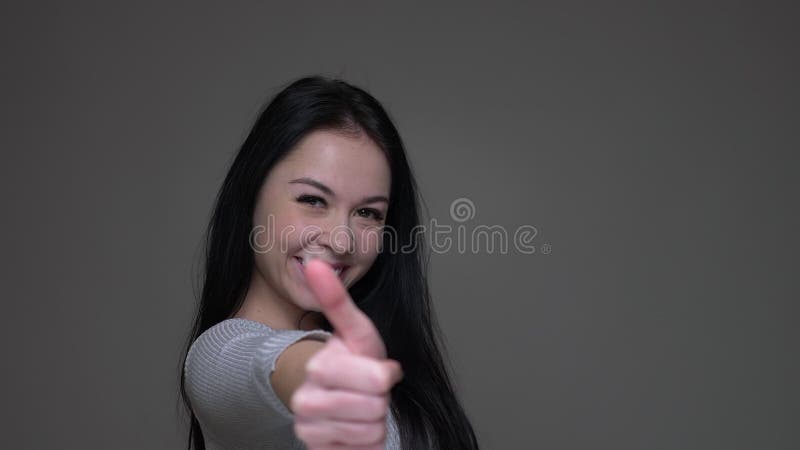 Closeup shoot of young pretty brunette caucasian female turning around with her hair fluttering showing thumb up with