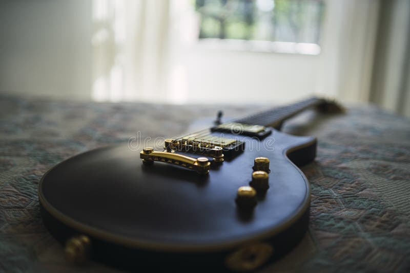 Closeup shot of a black electric guitar on a bed with patterned sheet stock photo