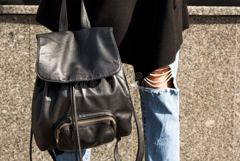 Closeup shot of black leather backpack at the woman`s legs