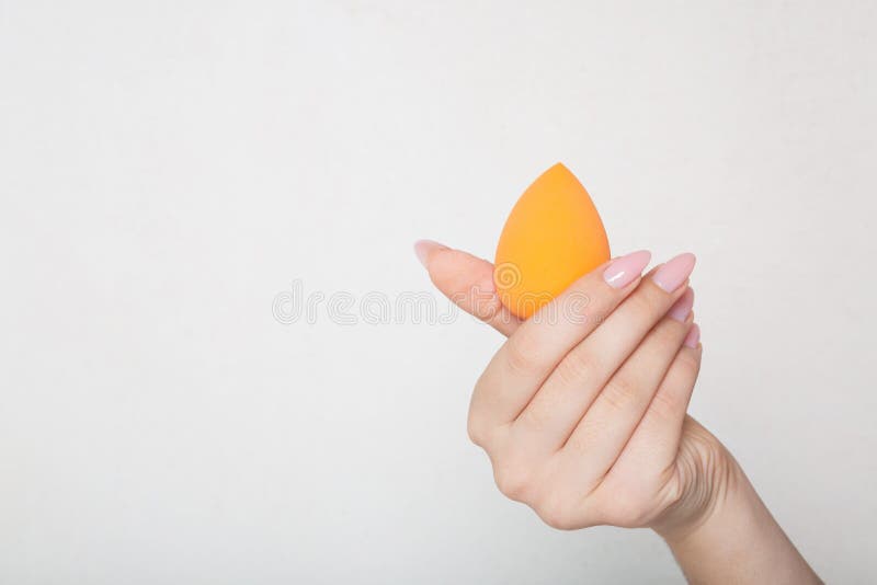 Closeup shot of female hand holding orange egg sponge over a white background. Empty space