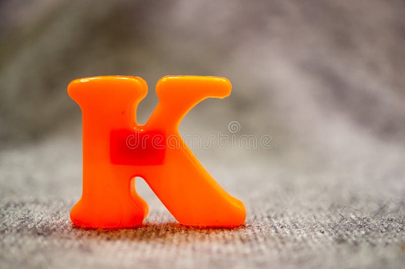 Closeup shot of a plastic orange-colored upper case letter 'K' on a playroom carpet stock image