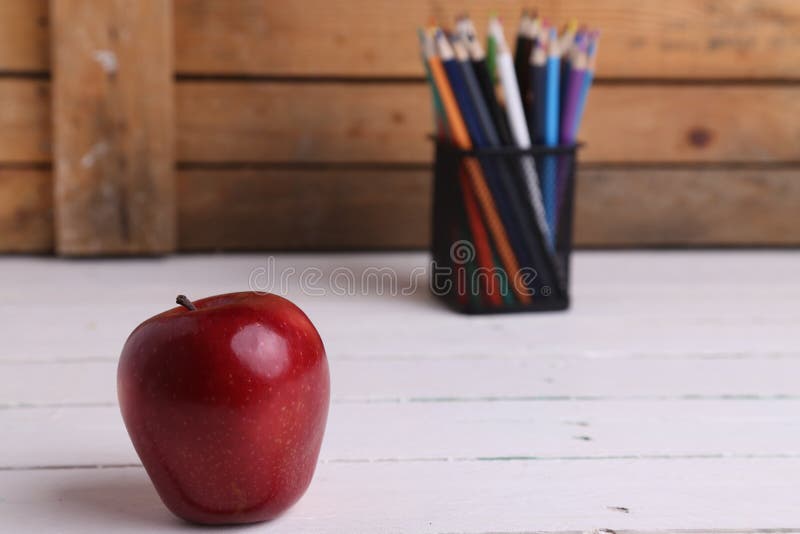 Closeup shot of a shiny apple and a jar of colorful pencils on a teachers desk