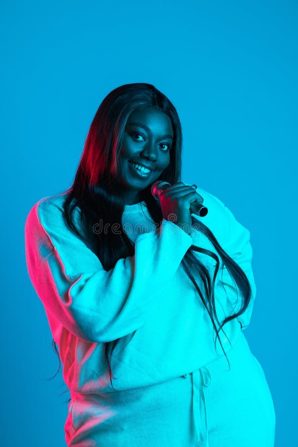 Close-up shot of African charming woman with long straight hair isolated on blue studio background in neon light. Concept of human emotions, facial expression, beauty, fashion. Bodypositive and diversity. Close-up shot of African charming woman with long straight hair isolated on blue studio background in neon light. Concept of human emotions, facial expression, beauty, fashion. Bodypositive and diversity