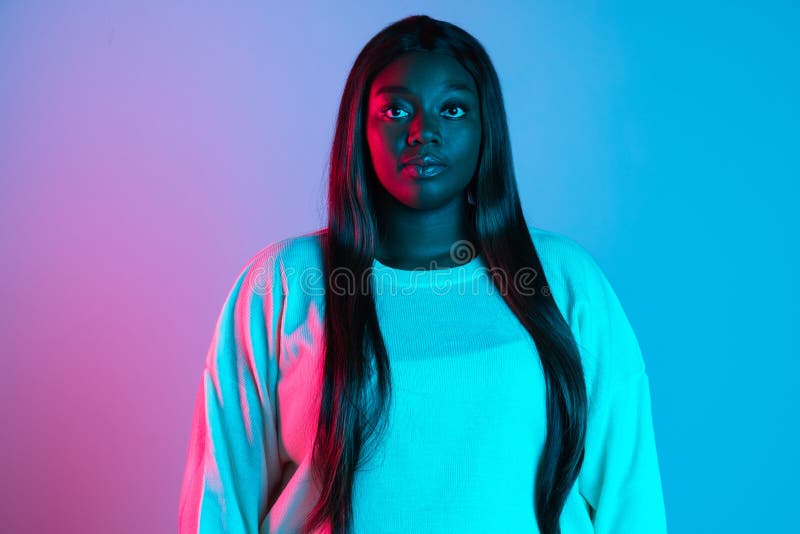 Calm, confident girl. African charming woman with long straight hair isolated on blue studio background in neon light. Concept of human emotions, facial expression. Bodypositive and diversity. Calm, confident girl. African charming woman with long straight hair isolated on blue studio background in neon light. Concept of human emotions, facial expression. Bodypositive and diversity