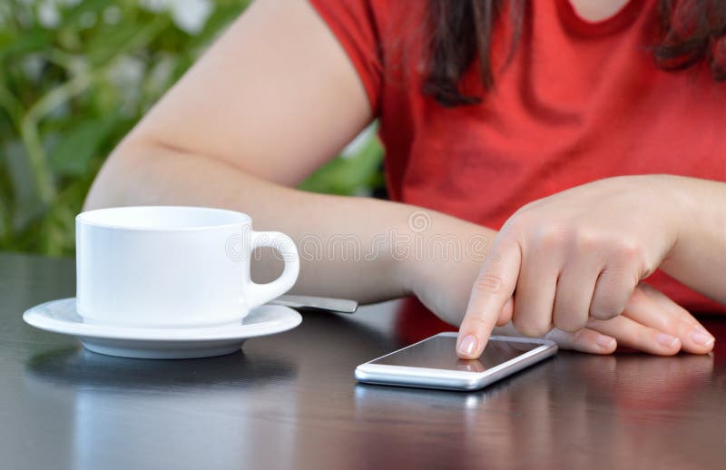 Young woman using a cellphone and drinking a coffee while sitting in a cafe royalty free stock photography Young woman using a cellphone and drinking a coffee while sitting in a cafe royalty free stock photography