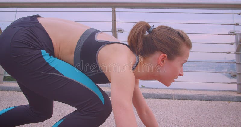 Closeup side view portrait of young caucasian sporty female jogger sitting in a start position and running on the bridge