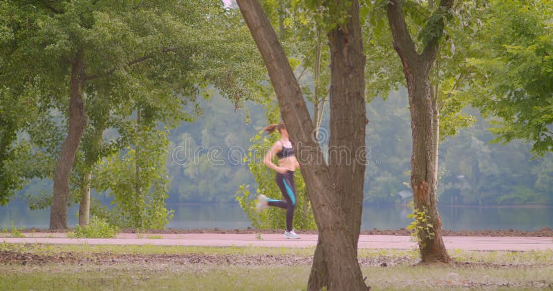 Closeup side view portrait of young pretty sporty female runner jogging in the park in urban city outdoors