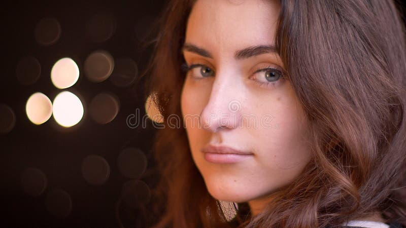 Closeup side view shoot of young attractive caucasian female face turning and looking at camera with bokeh lights on the background.