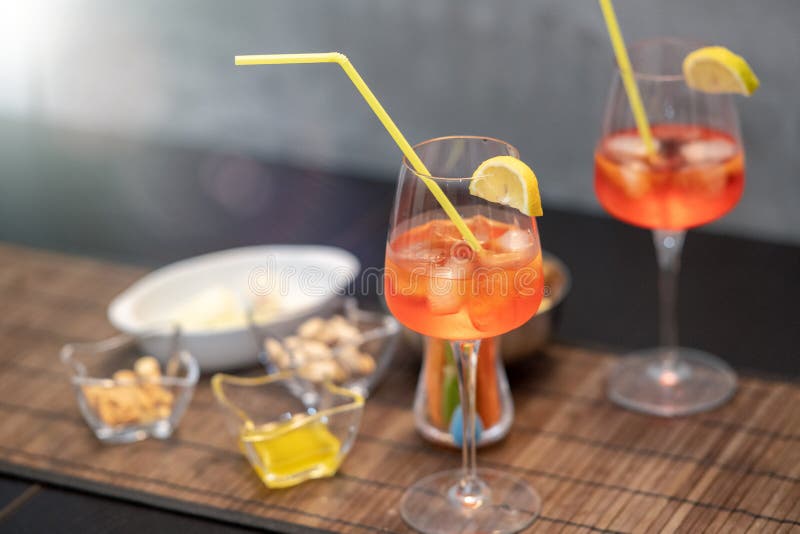 Closeup of some glasses with cocktails with  straws and nuts on a brown table