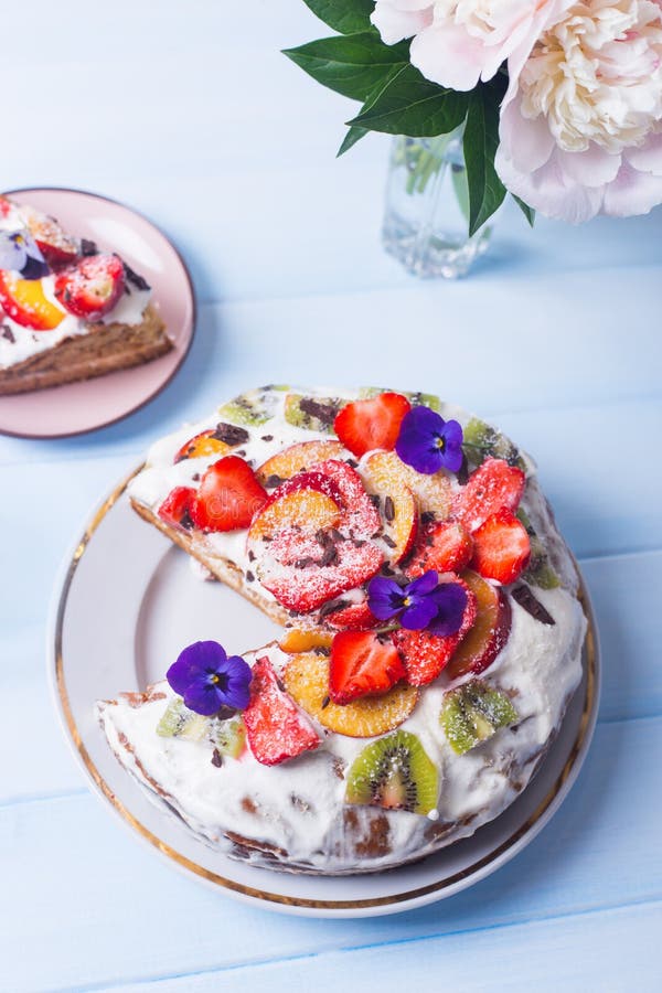 Closeup spring homemade sour cream fruit cake with coconut and chocolate flakes, kiwi,strawberry and peach, decorated with flowers