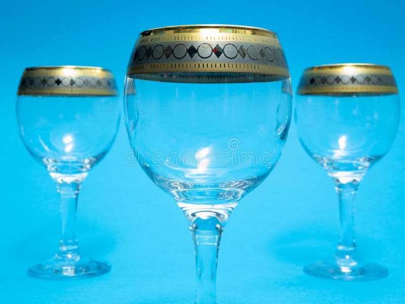 Closeup of three empty wine glasses, one up close to camera and two other on sides blurred on background. with blue backdrop