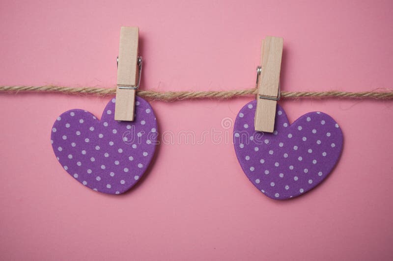Two purple hearts on clothespins on pink background - Valentine`s day concept