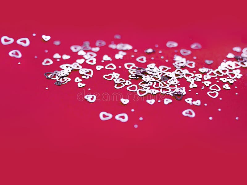 Closeup view of a few silver hearts arranged on paper on a red background. Valentines day. Symbol.