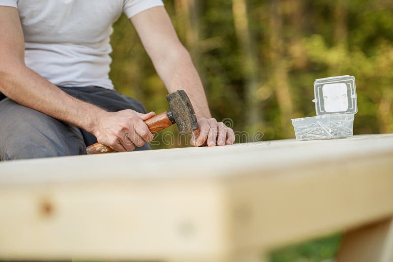 Closeup view of a man using a mallet to hammer a nail in a wooden playhouse stock image
