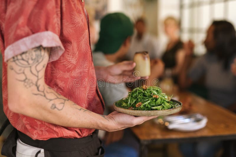 Waiter serving salad to customers sitting at a restaurant table