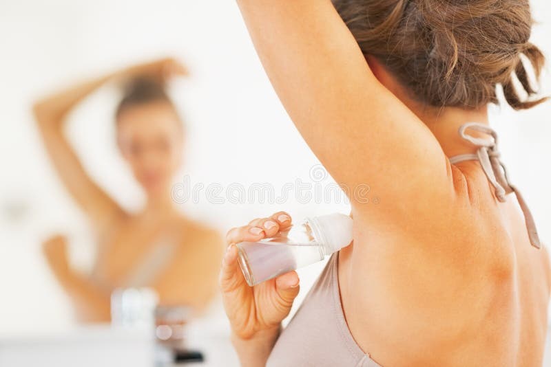 Closeup on young woman applying roller deodorant on underarm