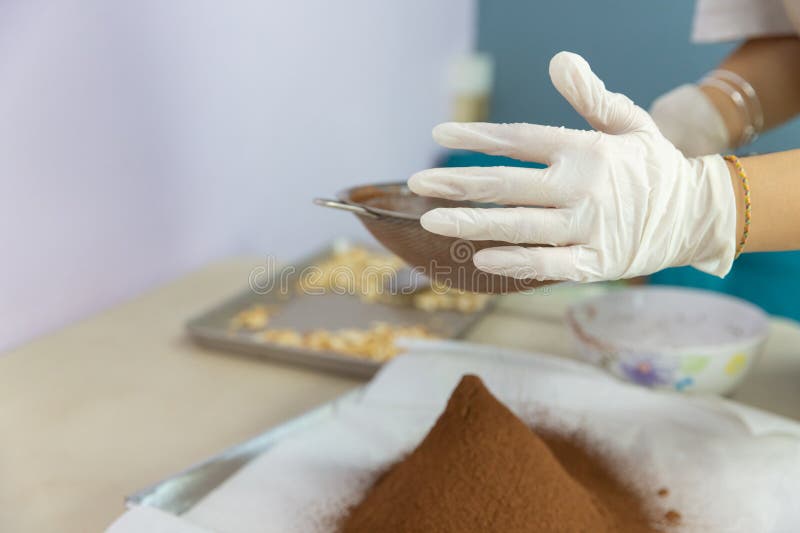 Closeup of woman, female baker hands while using flour sifter to make cocoa to bake homemade cake or bakery first time, learning stock photos
