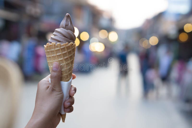 Closeup woman hand holding chocolate ice cream on walking street, selective focus.