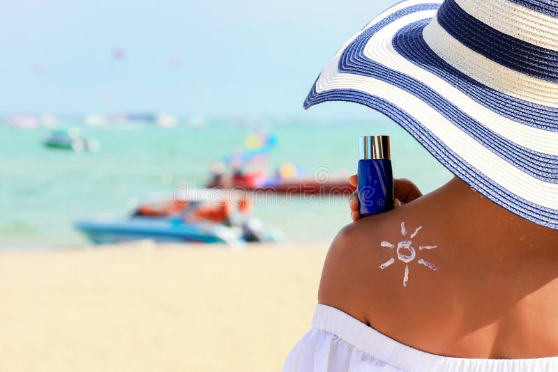 Closeup woman holding the sunblock bottle cream in hand, with sunblock lotion cream applied to her back and draw is the sun, at