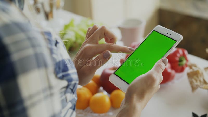 Closeup of woman`s hand browsing smartphone with green screen on kitchen at home royalty free stock photo Closeup of woman`s hand browsing smartphone with green screen on kitchen at home royalty free stock photo
