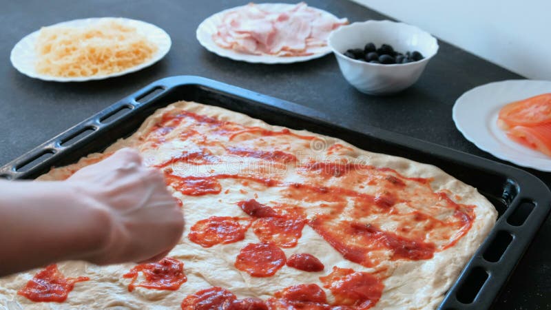 Closeup woman`s hands spreading sauce on pizza dough and smear it with spoon.