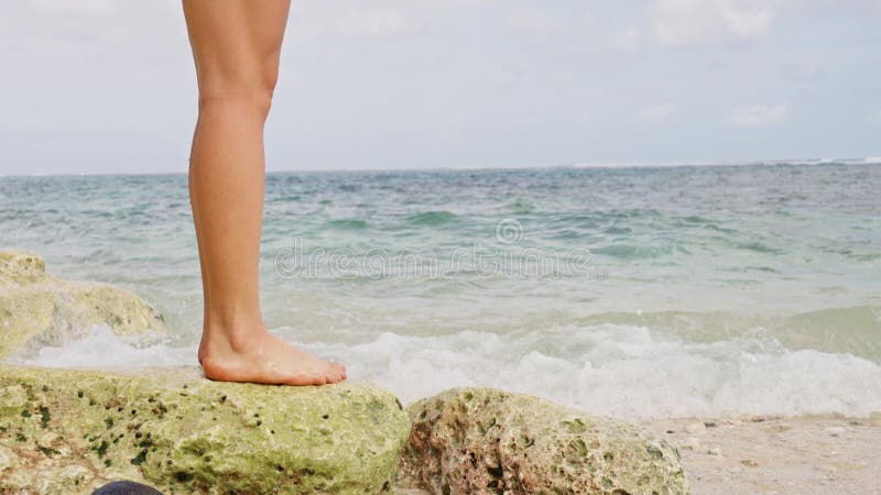 Closeup of a womans jambes une femme sur la pierre près de l'océan ralenti banque de vidéos