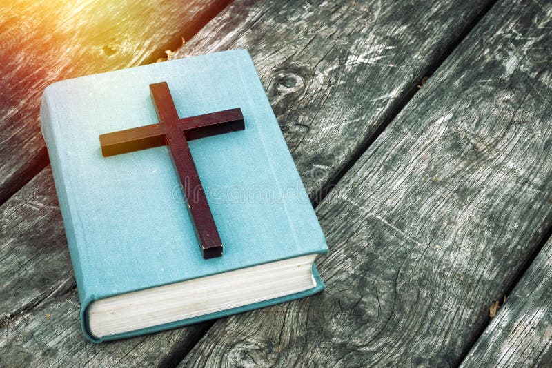 Closeup of wooden Christian cross on bible, burning candle and prayer beads on the old table.