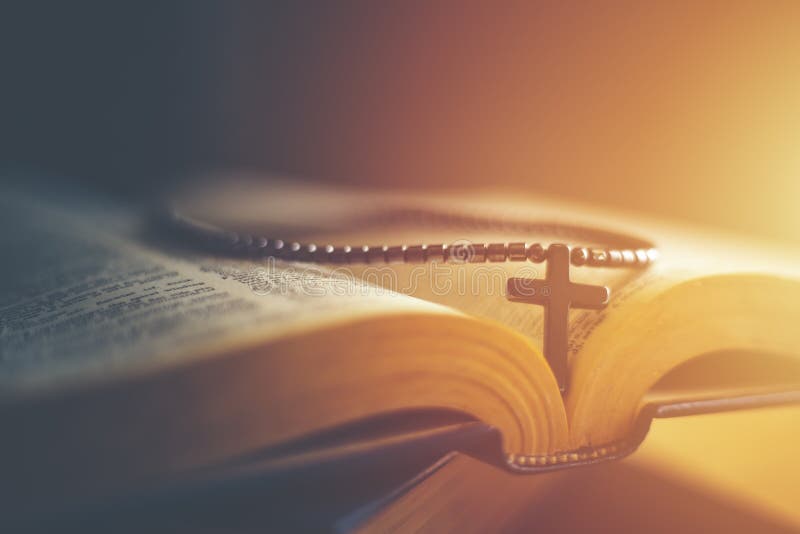 Closeup of wooden Christian cross necklace next to holy Bible .