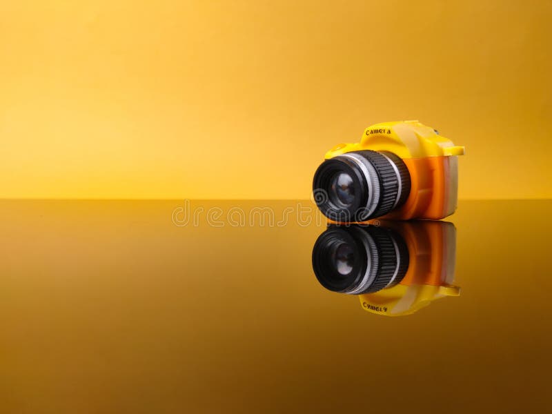 Closeup yellow camera on yellow background with reflection on a black acrylic board stock photo