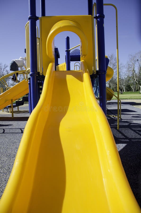 Closeup of a Yellow Playground Slide in a Park Surrounded by Greenery Under a Blue Sky and