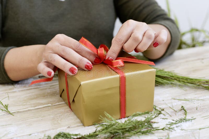 Woman tying a red ribbon around a gift. 