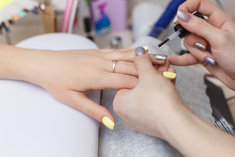 Closeupen av härligt applicera för händer som är genomskinligt, spikar polermedel i skönhetsalong ManikyristHand Painting Client arkivfoto Closeupen av härligt applicera för händer som är genomskinligt, spikar polermedel i skönhetsalong ManikyristHand Painting Client arkivfoto