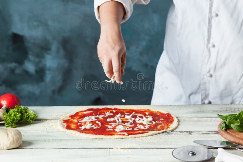 Closeuphand av kockbagaren i vit enhetlig danandepizza på kök