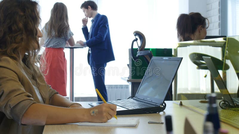 Closeupkvinnan arbetar på bärbar datorkollegor i bakgrund