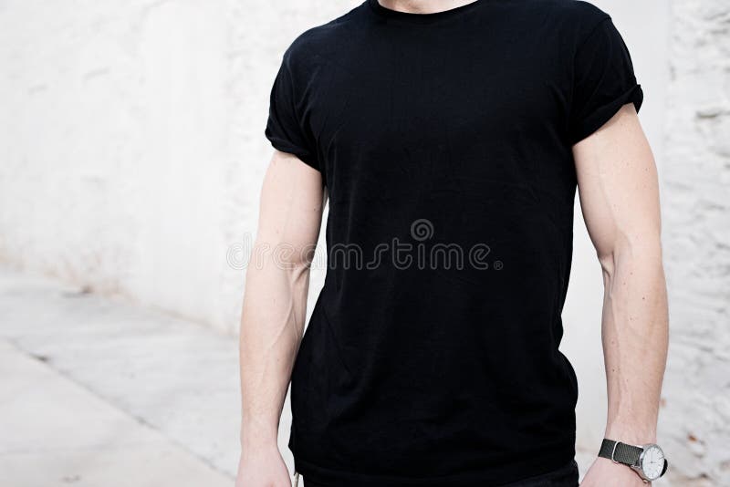 Closeupsikt av den unga muskulösa mannen som bär den svarta tshirten och jeans som utanför poserar Tom vit vägg på bakgrunden arkivbild Closeupsikt av den unga muskulösa mannen som bär den svarta tshirten och jeans som utanför poserar Tom vit vägg på bakgrunden arkivbild