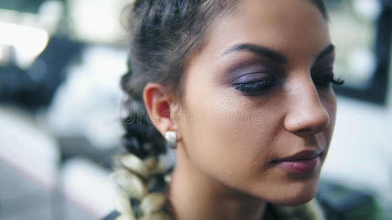 Closeupsikt av sammanträde för ung kvinna i skönhetstudion, medan makeupkonstnären korrigerar ögonbryn genom att använda sakkunni