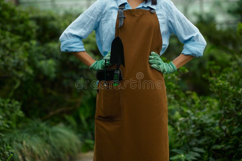 Closeup female gardener in overalls with garden small shovel and rake tool in pocket. Gardening and farming hobby concept. Closeup female gardener in overalls with garden small shovel and rake tool in pocket. Gardening and farming hobby concept