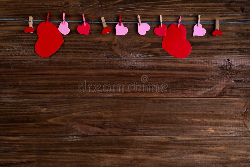 Clothespins με τις κόκκινες καρδιές σε μια κορδέλλα ως σύνορα σε ένα καφετί ξύλινο υπόβαθρο με το διάστημα για το κείμενο Η έννοι