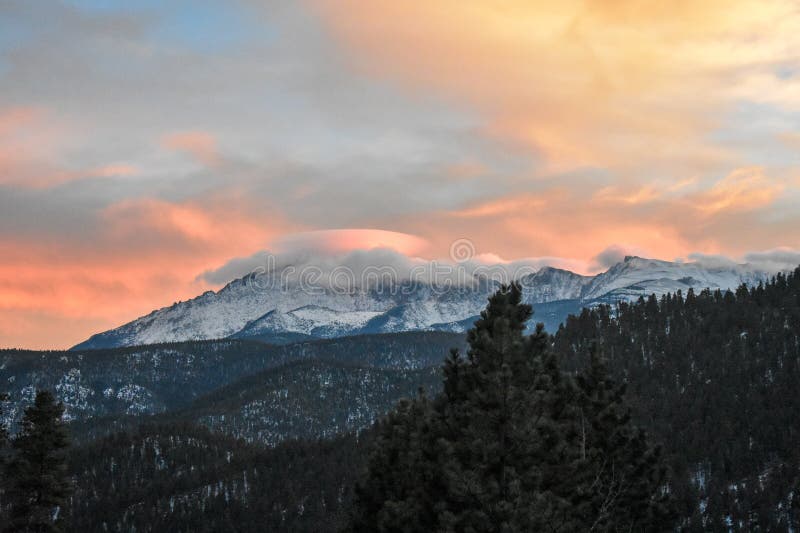 A dome of clouds formed over the top of Pike`s peak and sunset colors seen from Woodland Park, Colorado. Pike`s Prak os a fourteener located in Pike National Forest near Colorado Springs named in honor of America Explorer Zebulon Pike. Part of the Front Range of the Rocky Mountains in North America. Colorful clouds reflecting the setting sun. Freshly fallen snow on the trees and rocks of the mountain. A dome of clouds formed over the top of Pike`s peak and sunset colors seen from Woodland Park, Colorado. Pike`s Prak os a fourteener located in Pike National Forest near Colorado Springs named in honor of America Explorer Zebulon Pike. Part of the Front Range of the Rocky Mountains in North America. Colorful clouds reflecting the setting sun. Freshly fallen snow on the trees and rocks of the mountain.